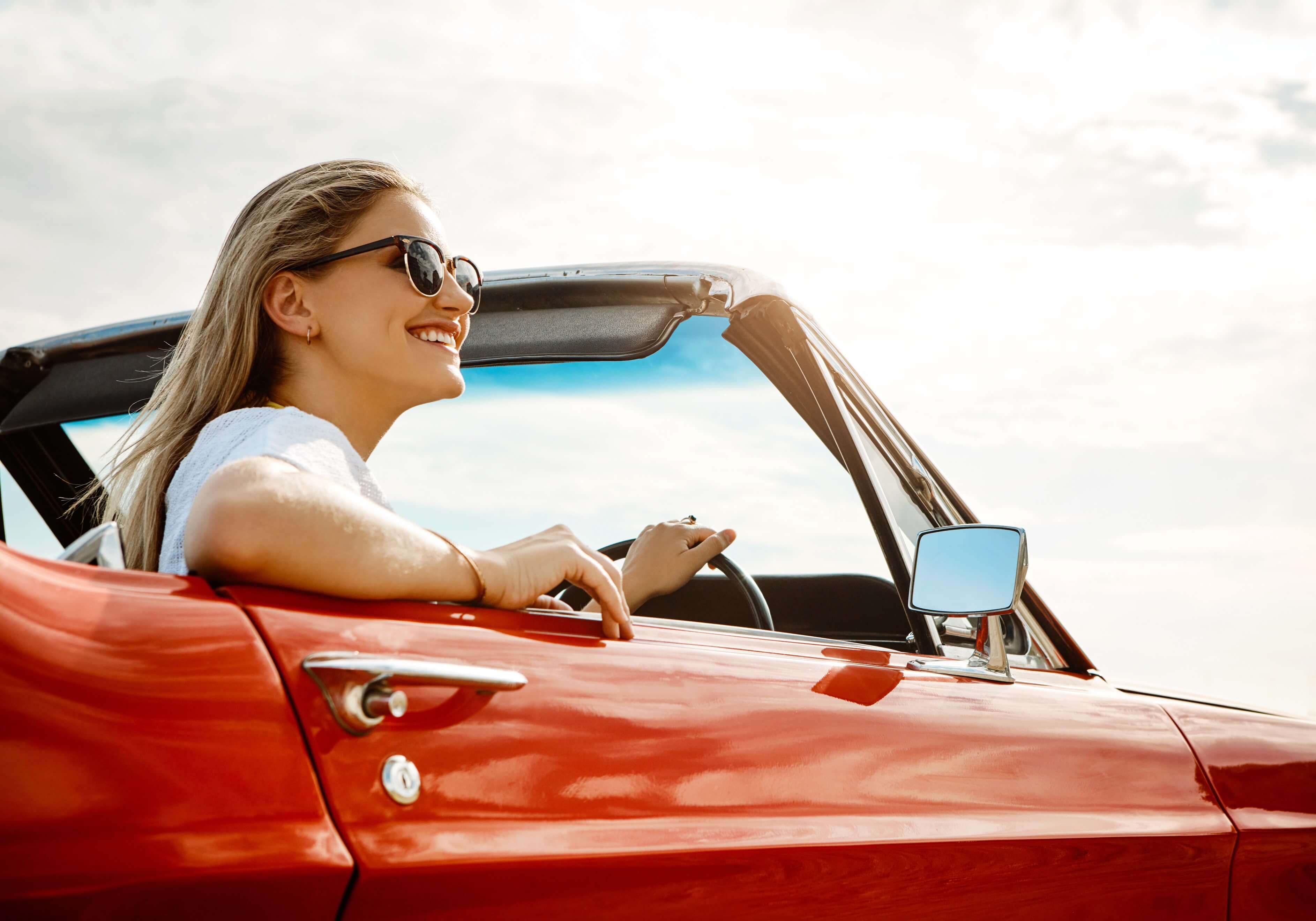 A smiling girl behind the wheel inside a convertible car