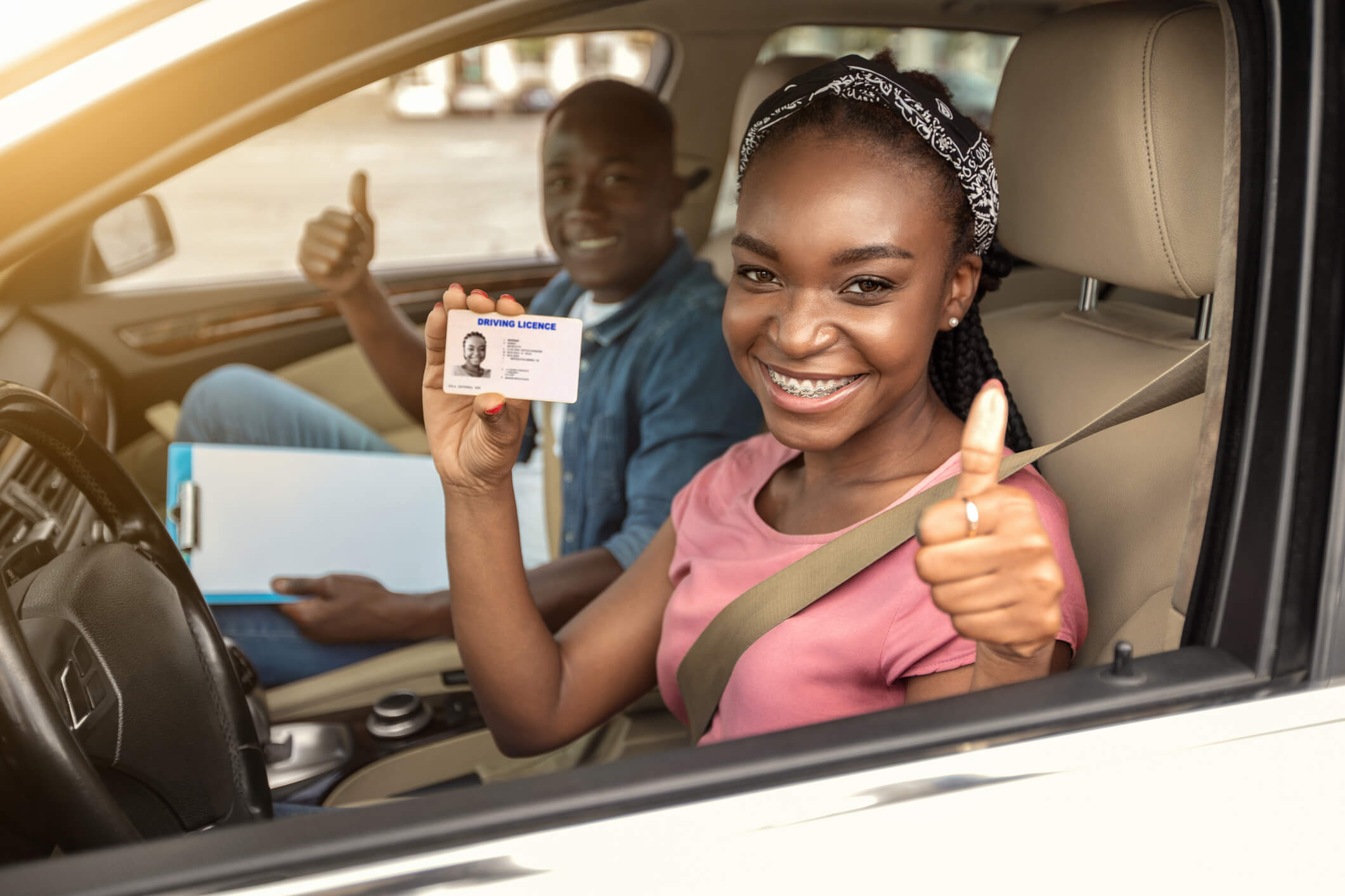 A girl showing her driver's license and cheering behind the wheel